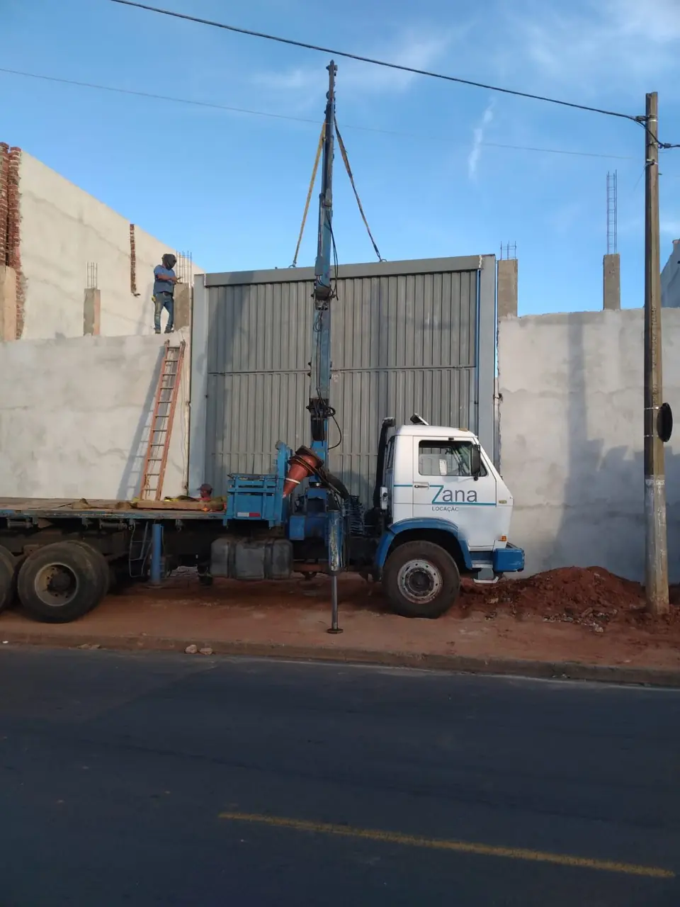 Caminhão munck da Zana visto de lado, com patolas abertas, instalando portão de galpão