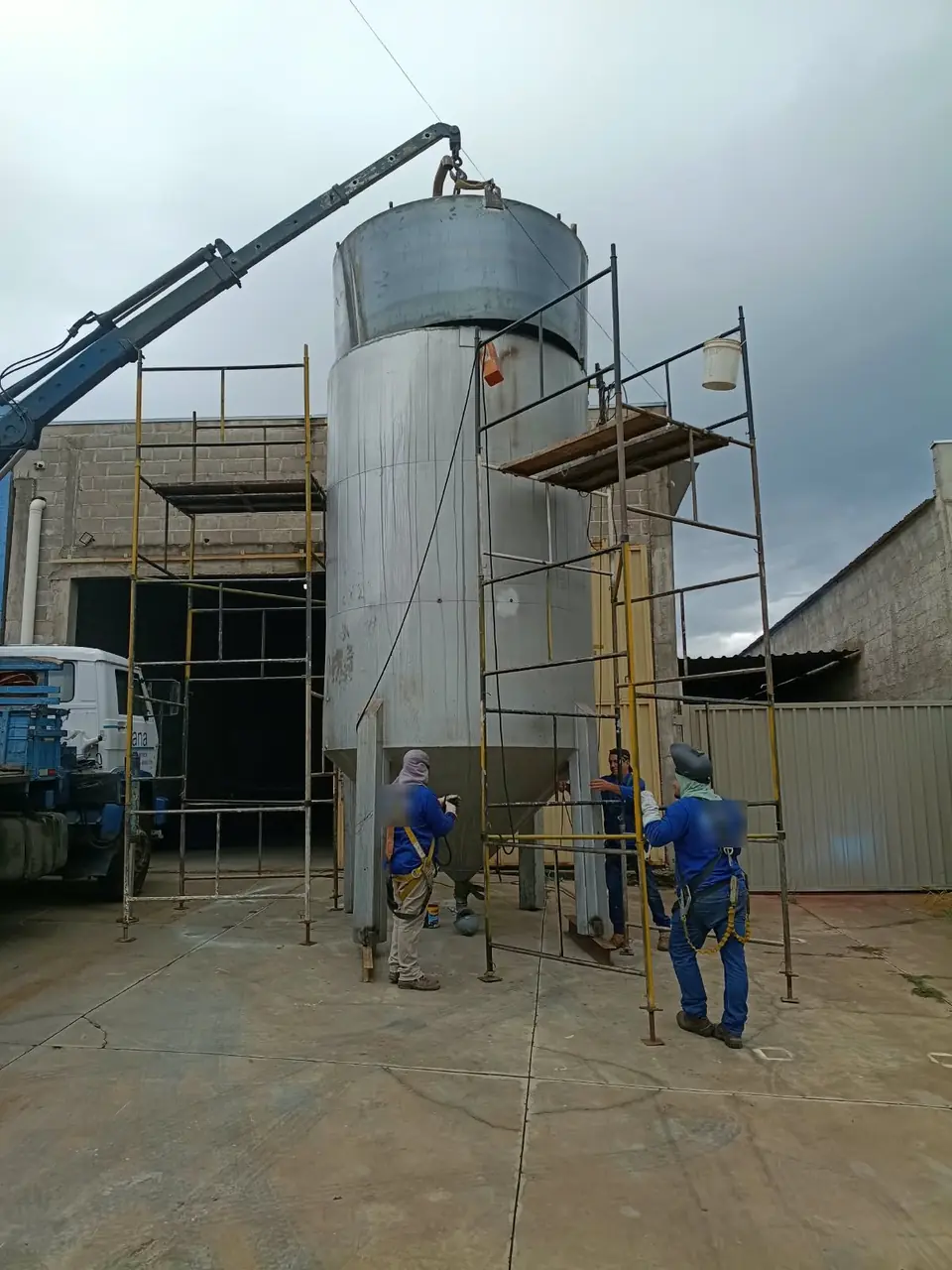 Equipe com cinto de segurança posicionando silo de inox içado pelo caminhão munck da Zana